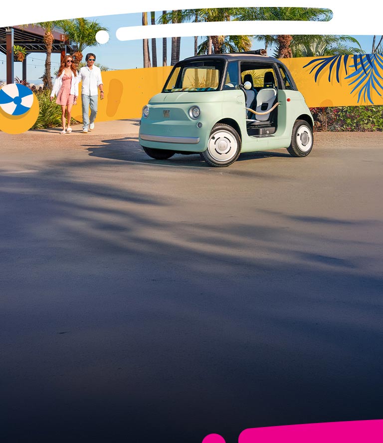 A mint green preproduction model Fiat Topolino Dolce Vita with door ropes and a rolled-up soft top, parked in the driveway of a resort, with a couple walking toward the vehicle.