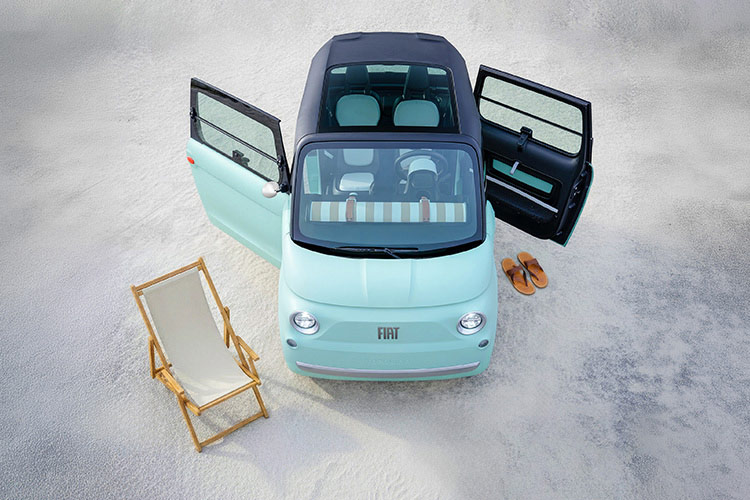 An overhead angle of a mint green preproduction model Fiat Topolino with its asymmetrical doors and glass sunroof open and beach accessories nearby.