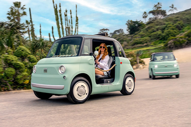 A woman driving a mint green preproduction model Fiat Topolino Dolce Vita down a hill, with a second Topolino following behind.