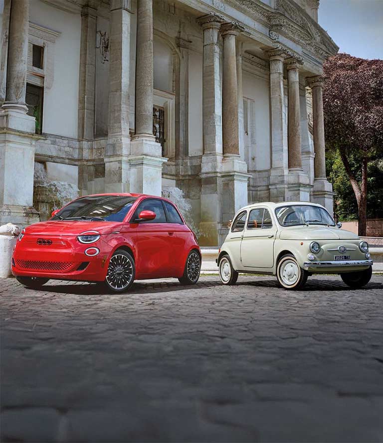 Un Fiat 500e Inspired y un Topolino clásico estacionados uno al lado del otro frente a una estructura.