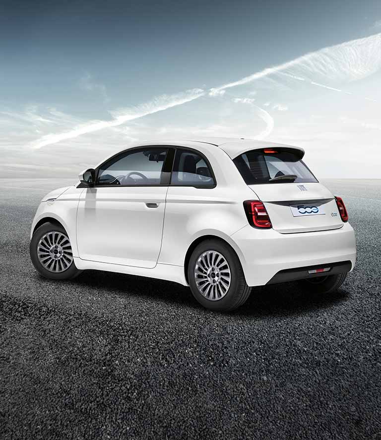 Perfil trasero en ángulo, del lado del conductor, de un Fiat 500e blanco, modelo europeo, de 2024, aparcado sobre grava.