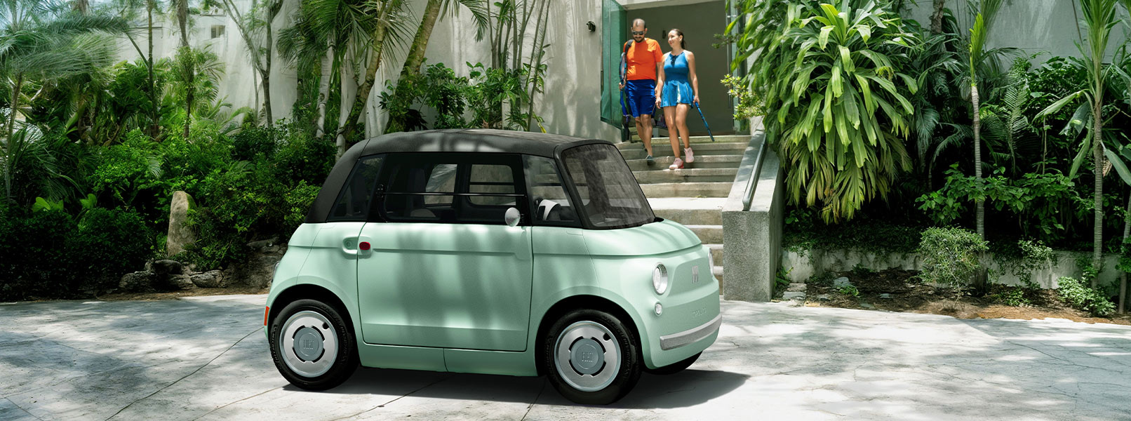A mint green preproduction model Fiat Topolino parked in front of a tennis club, with a couple exiting the club.